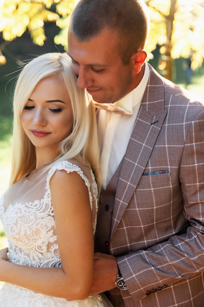 Joven pareja disfrutando de momentos románticos mientras camina en el parque. Elegante novia y el novio posando y besándose en el parque el día de su boda. Elegante novia en un hermoso vestido blanco, el novio en un traje.