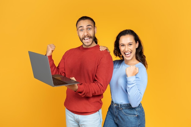 Una joven pareja emocionada sosteniendo y usando una computadora portátil