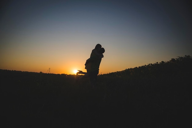 Una joven pareja enamorada al fondo de una puesta de sol en un campo