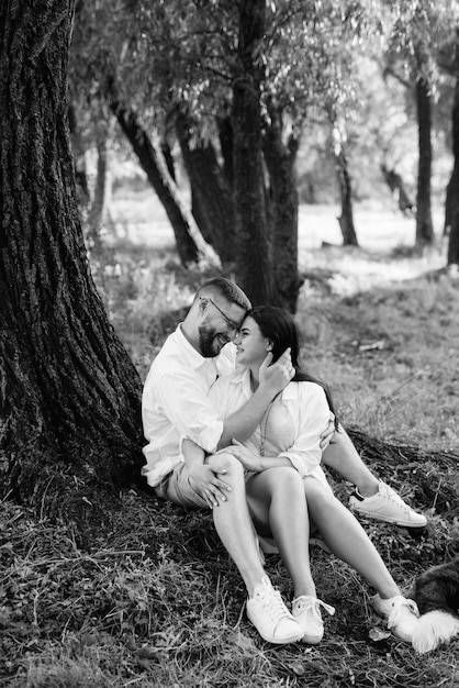 Joven pareja enamorada de un chico con barba y una chica de cabello oscuro con ropa clara en el bosque verde