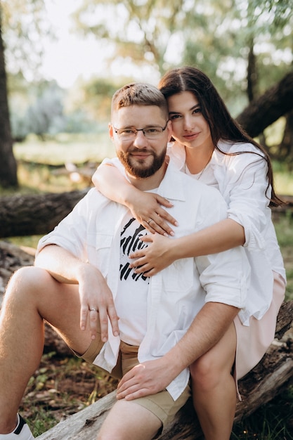 Joven pareja enamorada de un chico con barba y una chica de cabello oscuro con ropa clara en el bosque verde