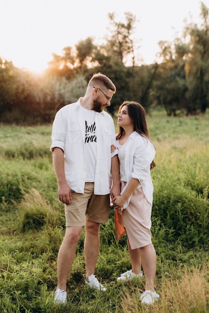 Joven pareja enamorada de un chico con barba y una chica de cabello oscuro con ropa clara en el bosque verde