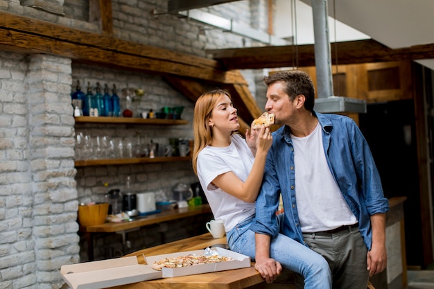 Joven pareja enamorada comiendo pizza en la casa rústica