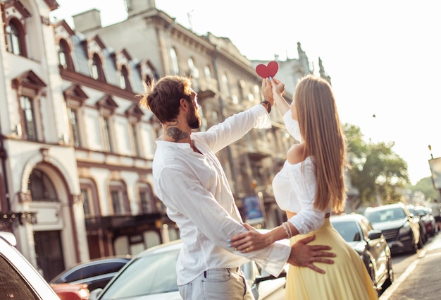 Una joven pareja enamorada con un corazón rojo mostrando su amor en la ciudad