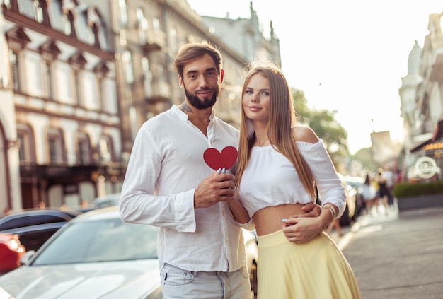 Una joven pareja enamorada con un corazón rojo mostrando su amor en la ciudad