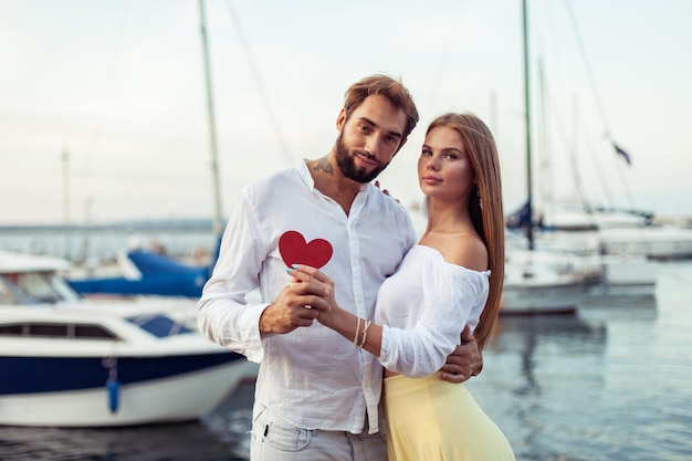 Foto una joven pareja enamorada con un corazón rojo mostrando su amor en un club de yates concepto romántico