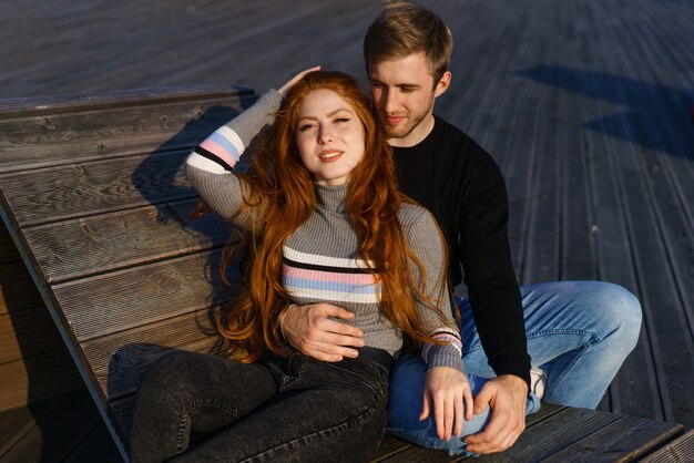 Una joven pareja enamorada de un hombre y una mujer se abrazan en un banco del área recreativa una hermosa redha ...