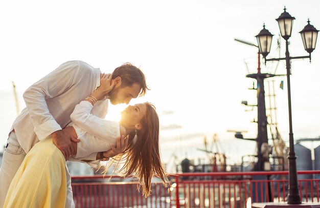 Joven pareja enamorada hombre y mujer besándose al atardecer en el puerto concepto de amor romántico