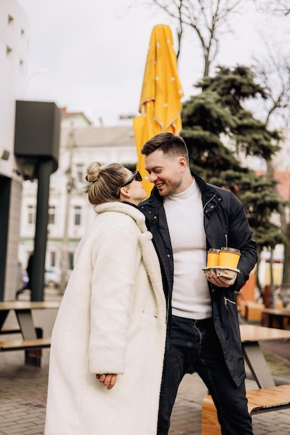 Una joven pareja enamorada en otoño en ropa de abrigo camina por la calle y bebe café Recreación al aire libre Pareja joven con estilo