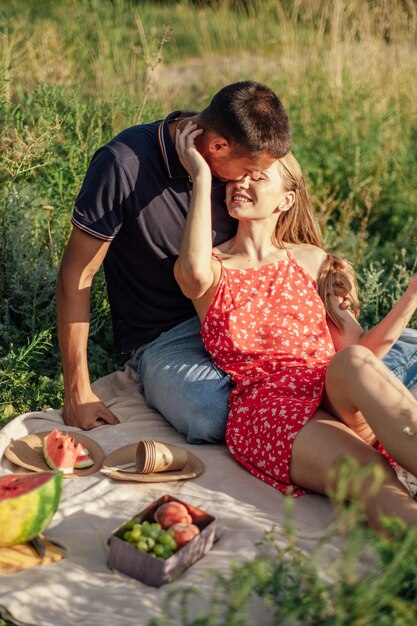 Joven pareja enamorada en un picnic de verano con una pareja amorosa de sandía sentada junto al río hablando