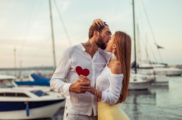 Una joven pareja enamorada que se besa con un corazón rojo mostrando su amor en el club de yates concepto de amor romántico