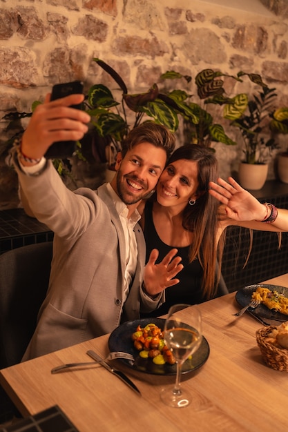Una joven pareja enamorada en un restaurante, divertirse cenando juntos, celebrando el Día de San Valentín, tomando un selfie de recuerdo