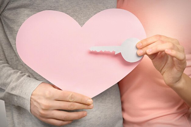 Joven pareja enamorada sosteniendo papel rosa corazón y llave de cerca
