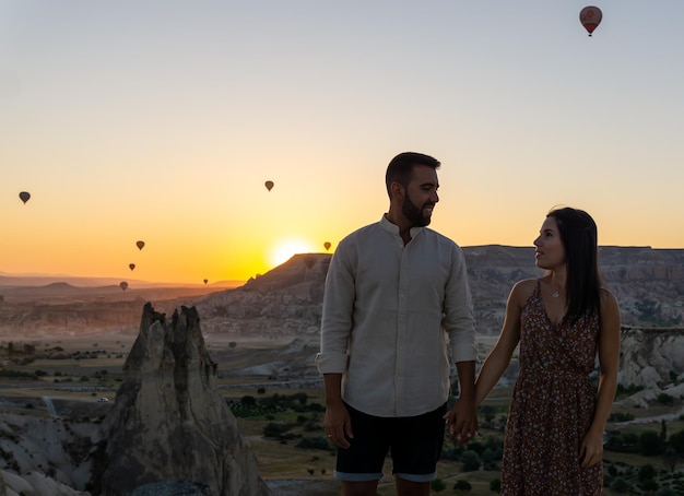 Joven pareja enamorada de turistas al amanecer en Capadocia con globos en el cielo