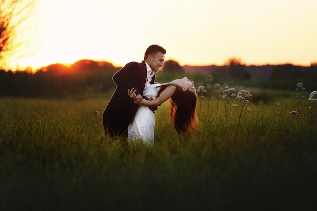 Joven pareja de enamorados se abrazan y se divierten al aire libre en el campo al atardecer el día de verano.