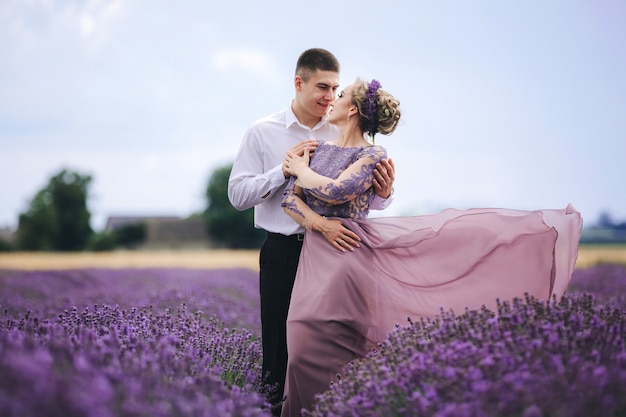 Joven pareja de enamorados abrazándose y caminando en un campo de lavanda en verano