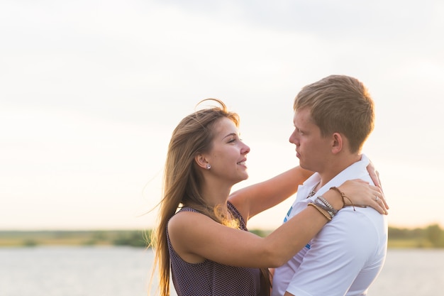 Joven pareja de enamorados al aire libre abrazándose y riendo juntos en el lago.