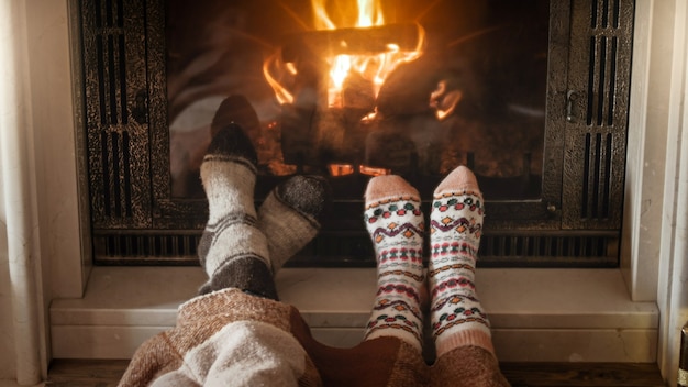 Joven pareja de enamorados en calcetines calientes de punto acostado junto a la chimenea en la sala de estar