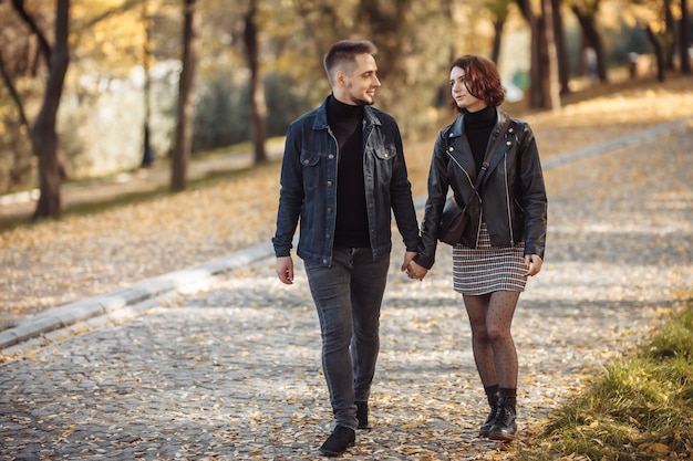 Joven pareja de enamorados caminando en el parque de la ciudad de otoño cogidos de la mano