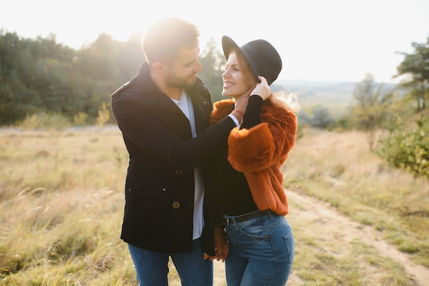 Joven pareja de enamorados caminando en el parque de otoño cogidos de la mano mirando la puesta de sol