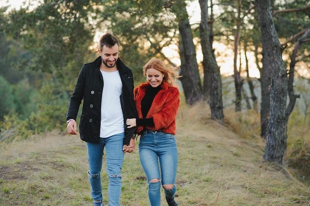 Joven pareja de enamorados caminando en el parque de otoño cogidos de la mano mirando la puesta de sol