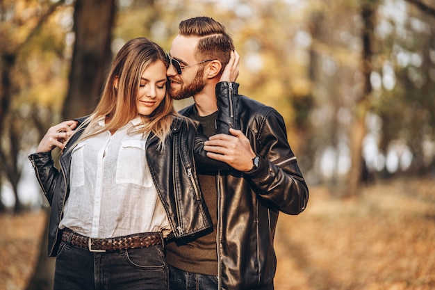 Una joven pareja de enamorados caminando en el parque otoño en un día soleado. El hombre abraza suavemente a la mujer. Historia de amor