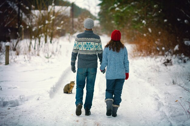 Joven pareja de enamorados cogidos de la mano caminando por la carretera nevada en la aldea