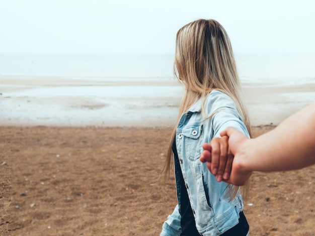 Joven pareja de enamorados cogidos de la mano están caminando por la playa contra la orilla del mar en la niebla. Familia joven feliz. Concepto de viajes y vacaciones.