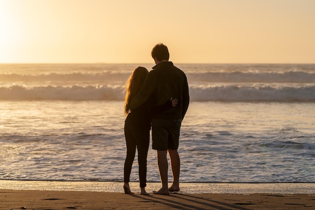 Joven pareja de enamorados enormes mutuamente en la playa viendo la puesta de sol