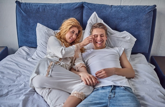 Joven pareja de enamorados está acostada en la cama, sonriendo y jugando.