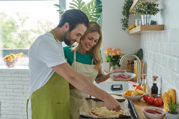 Una joven pareja de enamorados haciendo pizza casera mientras están juntos en la cocina