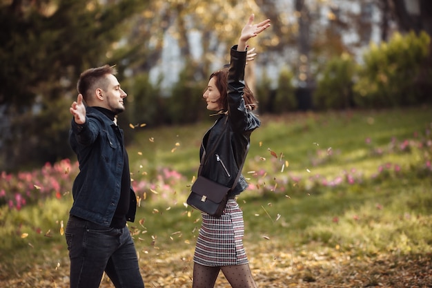 Joven pareja de enamorados jugando tirando hojas caídas en el parque de otoño