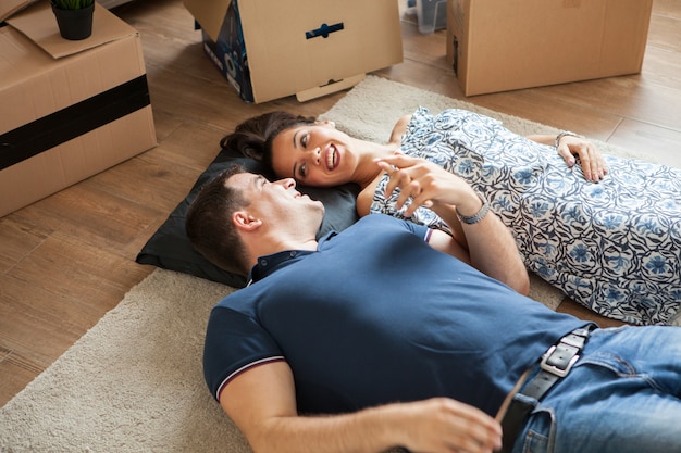 Joven pareja de enamorados mudarse en su nuevo apartamento. Acostados en el suelo uno al lado del otro y haciendo planes para su futuro