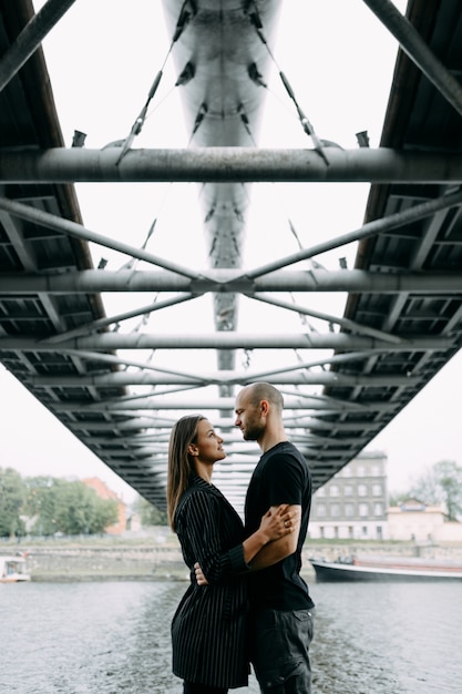 Joven pareja de enamorados de pie en el puente colgante de montaña abrazando mirando el uno al otro sonriendo