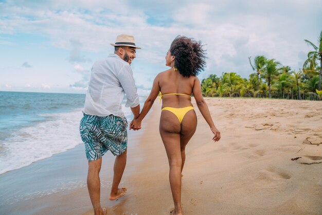 Joven pareja de enamorados en la playa, vacaciones de verano, feliz y sonriente cogidos de la mano