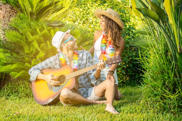 Joven pareja de enamorados sentados en el césped tocando la guitarra. concepto de amor y felicidad