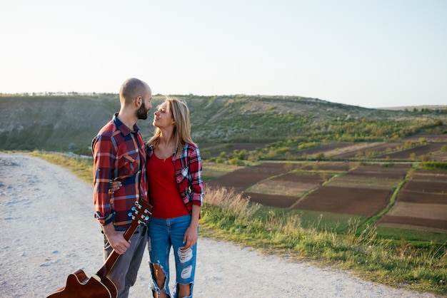 Joven pareja de enamorados sentados en el parque mientras estos jóvenes guitarra tocando la guitarra en el atardecer.