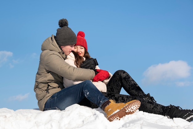 Joven pareja de enamorados se sienta en la nieve y abrazar. Cielo azul en el fondo.