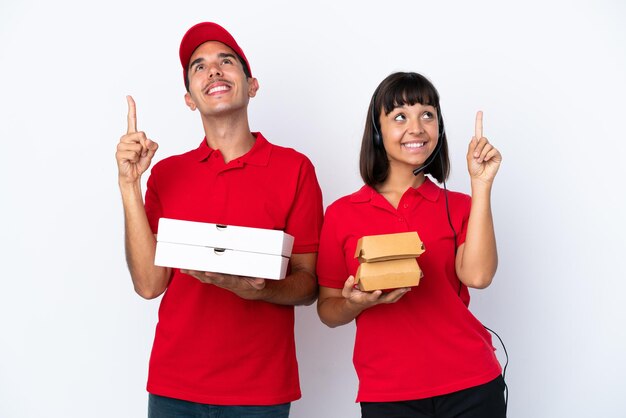 Joven pareja de entrega sosteniendo pizzas y hamburguesas aisladas sobre fondo blanco señalando con el dedo índice una gran idea