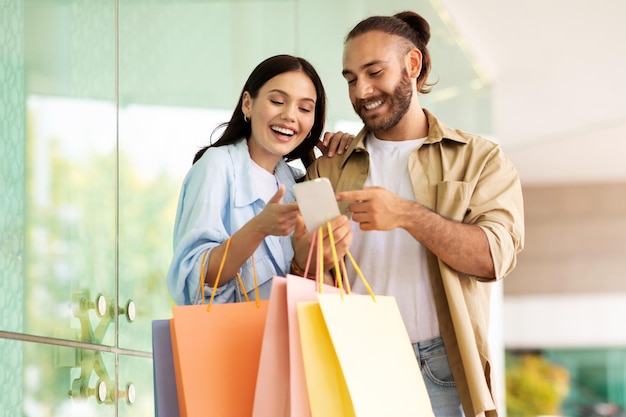 Una joven pareja europea alegre y sorprendida con bolsas disfruta de las compras y del tiempo libre mirando