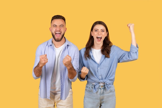 Foto una joven pareja en éxtasis celebra la victoria sobre un telón de fondo amarillo.