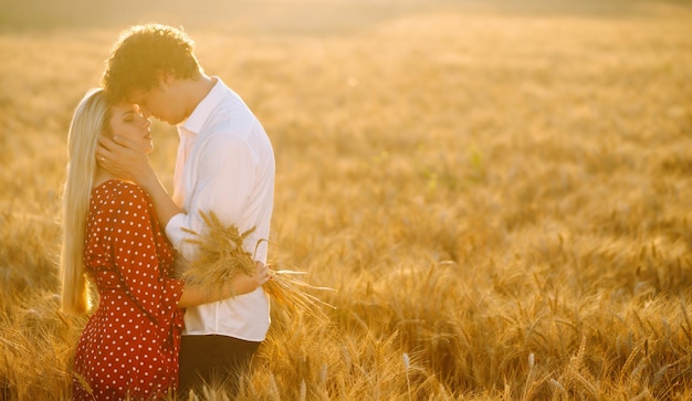 Joven pareja feliz abrazándose en un campo de trigo al atardecer Disfrutando el tiempo juntos