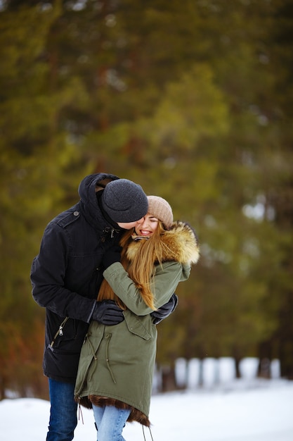 Joven pareja feliz abrazándose unos a otros en el bosque de invierno