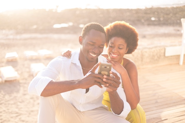 joven pareja feliz afroamericana raza afro multiétnica diversidad racial disfrutar de teléfono e internet en actividades de ocio al aire libre durante la brillante y dorada puesta de sol con luz. sonríe y quédate