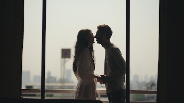 Joven pareja feliz besándose y disfrutando de la vista desde un balcón con vistas a la ciudad por la mañana