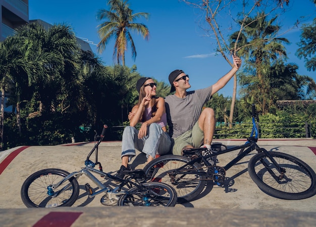 Joven pareja feliz con bmx tomándose selfie en el skatepark