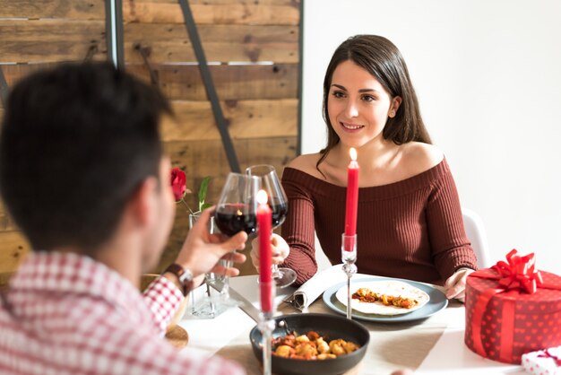 Foto joven pareja feliz celebrando el día de san valentín con una cena en casa bebiendo vino, aclamaciones.