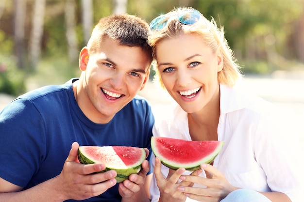 Una joven pareja feliz comiendo sandía en la playa.