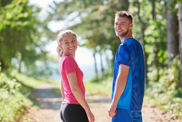 joven pareja feliz disfrutando de un estilo de vida saludable mientras trota en un camino rural a través del hermoso bosque soleado, el ejercicio y el concepto de fitness