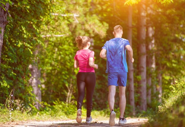 joven pareja feliz disfrutando de un estilo de vida saludable mientras trota en un camino rural a través del hermoso bosque soleado, el ejercicio y el concepto de fitness